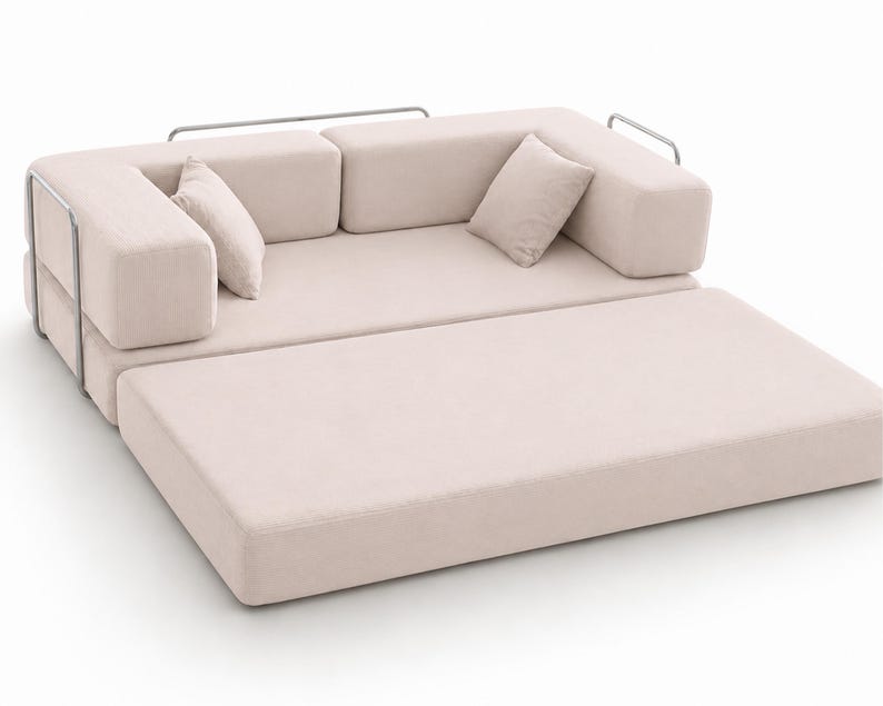 May include: A light beige modular sofa bed featuring a low-profile design with a metal frame, two square back cushions, and two smaller throw pillows. The base extends outward to create a flat sleeping surface, upholstered in a solid light fabric.