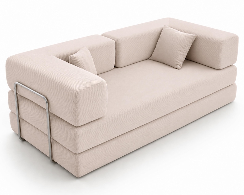 May include: A beige sofa with a textured fabric finish, featuring a low-profile design, thick rectangular armrests, and two matching square throw pillows. The structure is supported by a visible, thin, silver-toned metal frame on the side.