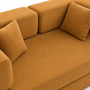 May include: A mustard yellow corduroy sofa featuring a textured ribbed fabric finish, thick rectangular armrests, and two matching square throw pillows placed on the seat. The furniture has a clean, blocky design with a uniform golden-brown color.