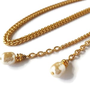May include: A gold chain necklace with two white pearl-like pendants. The chain is a double-layered design with a braided and a link chain.