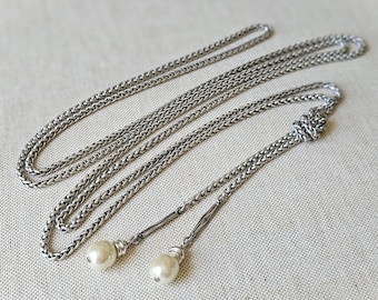 May include: A silver chain necklace with two pearl accents at the ends. The chain is a braided design and is long enough to be worn as a lariat.