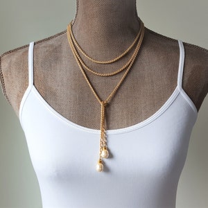 May include: A gold layered necklace with a long tassel and two pearl accents.