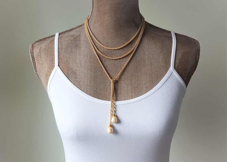 May include: A gold layered necklace with a long tassel and two pearl accents.