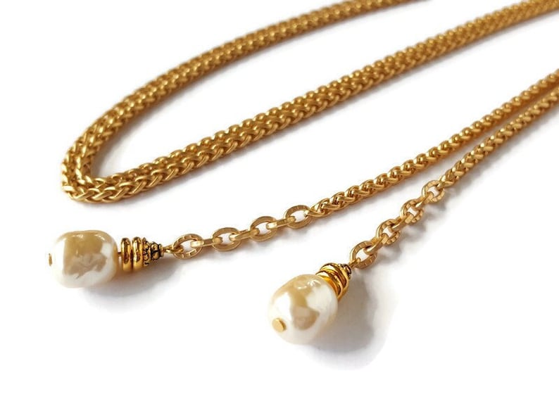 May include: A gold chain necklace with two white pearl-like pendants. The chain is a double-layered design with a braided and a link chain.