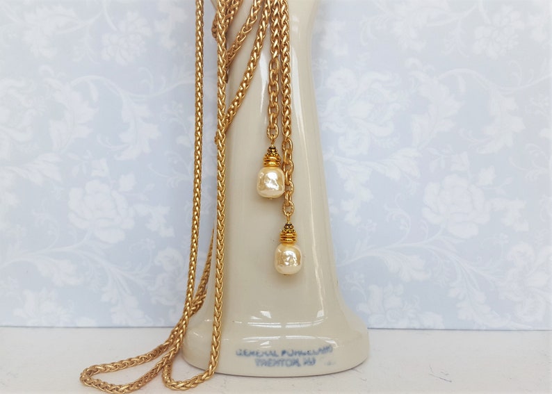 May include: A gold chain necklace with two pearl drops. The chain is braided and has a gold clasp.