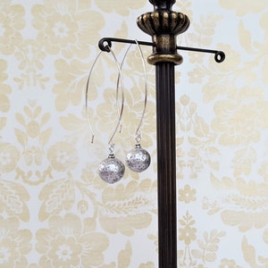May include: A pair of silver dangle earrings with hammered round silver beads. The earrings are hanging from a silver stand.