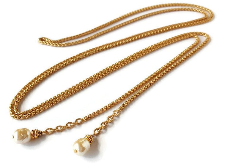 May include: A gold chain necklace with two pearl accents. The chain is a double strand of braided gold chain.