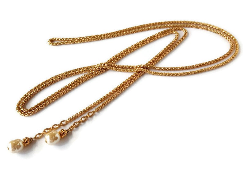 May include: A gold chain necklace with two white pearl accents. The chain is a braided design and is long enough to be worn as a lariat.