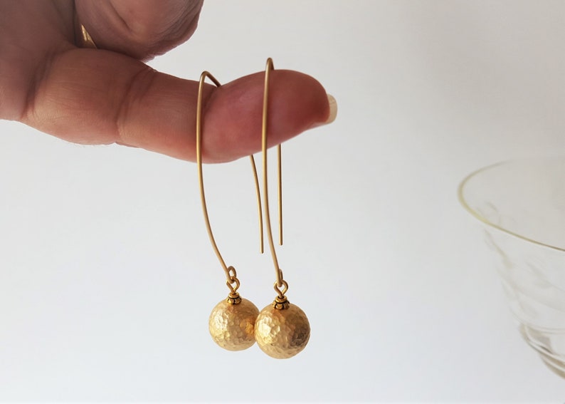 May include: A pair of gold dangle earrings with hammered ball charms. The earrings are made of brass and have a simple, elegant design.