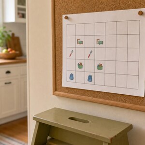 May include: A white paper grid chart pinned to a cork board with two wooden pins. The chart features small colorful icons of a bed, a toothbrush, a toy box, and a backpack. A small ceramic cup containing colorful star stickers is attached to the board.