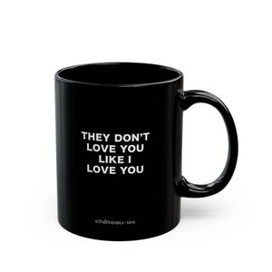 May include: Black ceramic mug with the text "THEY DON'T LOVE YOU LIKE I LOVE YOU" in white. The mug also has the text "château-104" in white at the bottom. The mug has a curved handle.