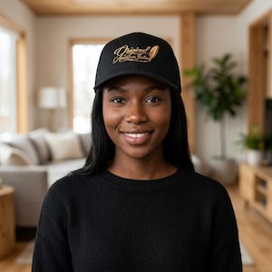 Puede incluir: Gorra de béisbol negra con el texto dorado "Original American Indian" y un diseño de pluma. La gorra la lleva una persona que lleva un jersey negro.