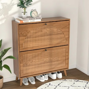 May include: A wooden shoe cabinet with two drop-down doors featuring a vertical slatted design and a semi-circular arch pattern on the top door. The cabinet stands on four tapered legs and includes small black knobs for opening each compartment.