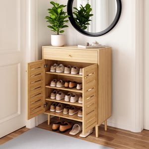 May include: A light wood shoe cabinet featuring a single top drawer and two louvered doors that open to reveal four interior shelves filled with various pairs of shoes. The cabinet stands on four tapered legs and has a smooth, natural wood grain finish.