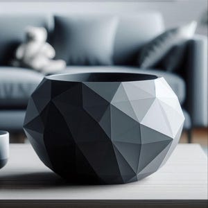 Pode incluir: Uma taça cinzenta escura com uma superfície geométrica facetada composta por múltiplos planos triangulares. O objeto apresenta uma abertura circular larga no topo e uma estrutura exterior arredondada e poligonal com ângulos vivos.