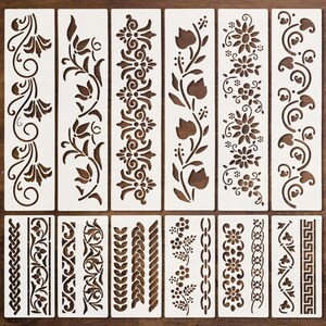Könnte beinhalten: Ein Set aus zwölf rechteckigen weißen Schablonen mit verschiedenen ausgeschnittenen Mustern, darunter Blumenranken, geometrische Bordüren, geflochtene Seile, Kettenglieder und griechische Mäander, angeordnet in zwei Reihen.