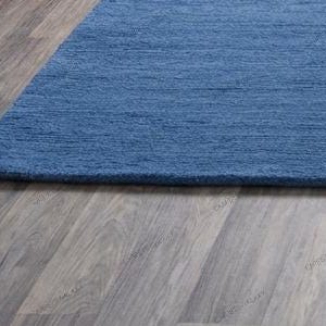 Solid blue hand-tufted wool rectangular area rug with medium Loop pile on wood flooring in a minimalist living room setting.