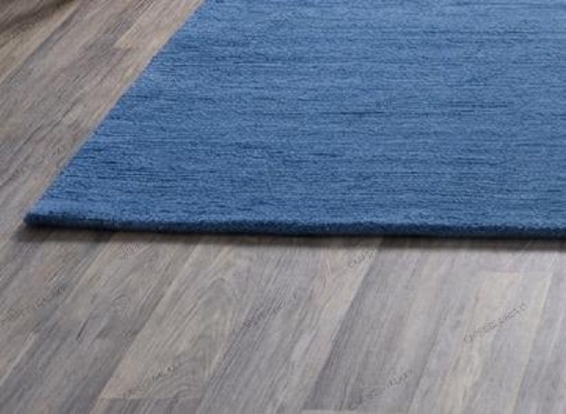Solid blue hand-tufted wool rectangular area rug with medium Loop pile on wood flooring in a minimalist living room setting.