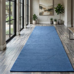Solid blue hand-tufted wool rectangular area rug with medium Loop pile on wood flooring in a minimalist living room setting.