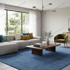 Solid blue hand-tufted wool rectangular area rug with medium Loop pile on wood flooring in a minimalist living room setting.