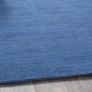 Solid blue hand-tufted wool rectangular area rug with medium Loop pile on wood flooring in a minimalist living room setting.