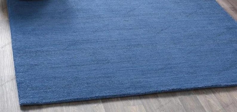 Solid blue hand-tufted wool rectangular area rug with medium Loop pile on wood flooring in a minimalist living room setting.