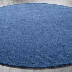 Solid blue hand-tufted wool rectangular area rug with medium Loop pile on wood flooring in a minimalist living room setting.
