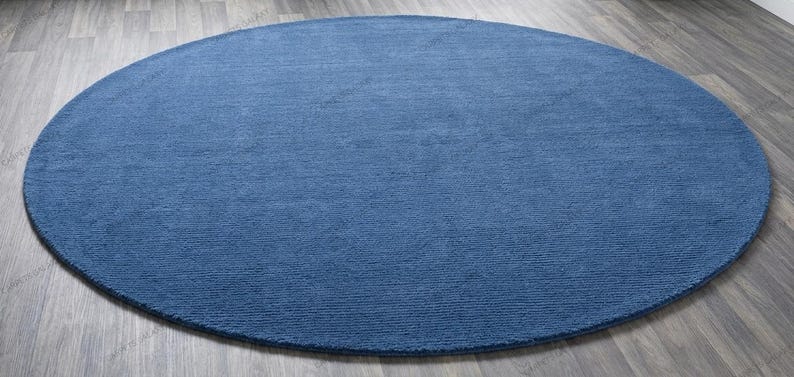 Solid blue hand-tufted wool rectangular area rug with medium Loop pile on wood flooring in a minimalist living room setting.