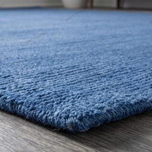 Solid blue hand-tufted wool rectangular area rug with medium Loop pile on wood flooring in a minimalist living room setting.