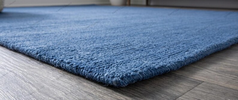 Solid blue hand-tufted wool rectangular area rug with medium Loop pile on wood flooring in a minimalist living room setting.