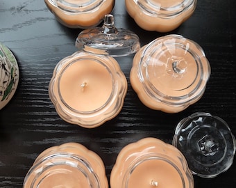 May include: A collection of pumpkin-shaped glass jars filled with light orange wax, each featuring a matching clear glass lid with a small handle. Some jars are closed, while others are open, revealing the central wick inside the wax.