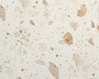 May include: A flat surface featuring a terrazzo pattern with an off-white base color. The design consists of scattered, irregular stone fragments in various shades of beige, tan, light brown, and soft gray, creating a speckled, multi-tonal texture.