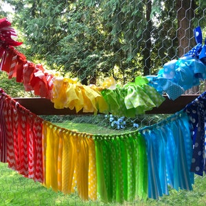 May include: A rainbow fabric garland with white polka dots, stripes, and chevron patterns. The garland is made of fabric scraps sewn together and has a frayed edge.