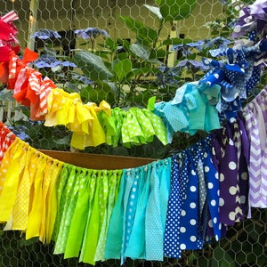 May include: A rainbow fabric garland with different patterns, including polka dots, stripes, and chevron. The garland is made of colorful fabric scraps and is perfect for a party or celebration.