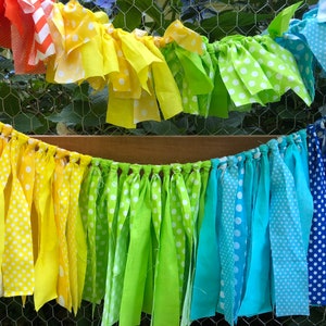 May include: A rainbow fabric banner with white polka dots and chevron patterns. The banner is made of strips of fabric tied together and hangs from a wooden dowel.