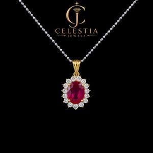 Könnte beinhalten: Eine goldene Anhängerkette mit einem oval geschliffenen, tiefroten Edelstein, der von einem Kranz aus kleinen, klaren Steinen umgeben ist, an einer silberfarbenen Kugelkette. Das Logo von Celestia Jewels ist über dem Anhänger zu sehen.