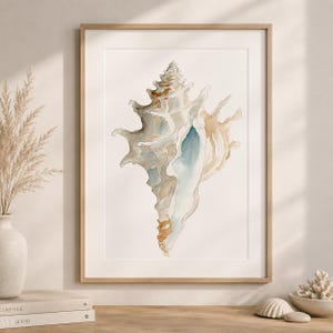 Puede incluir: Una lámina de acuarela enmarcada que presenta una ilustración detallada de una concha marina con espinas en tonos bronceado, marrón y azul suave. La obra está centrada sobre un fondo blanco en un marco de madera clara, mostrando texturas.