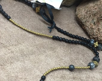 May include: A necklace with black and gold beads. The necklace has a variety of beads, including small gold beads, larger black beads, and larger gray beads with gold accents.