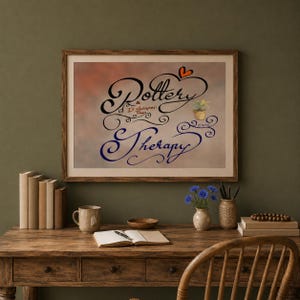 May include: A framed print with the words "Pottery is cheaper than Therapy" in elegant script. The artwork features a heart and a small potted plant. The print is displayed on a wooden desk with books, a mug, and a vase of flowers.
