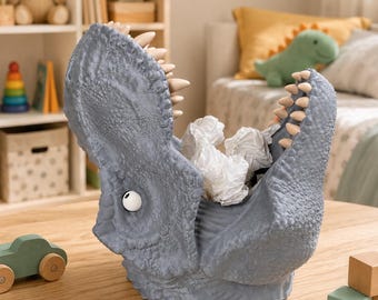 May include: A gray dinosaur-shaped wastebasket with a textured, scaly surface, a wide-open mouth featuring rows of pointed teeth, and a single visible white eye. The interior of the dinosaur's mouth is filled with crumpled white paper scraps.