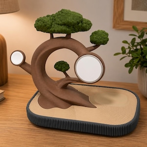 May include: A brown tree-shaped charging station with green foliage, featuring two circular white magnetic charging pads. The base is a rectangular tray with a tan, raked sand texture and a dark grey ribbed border, designed for electronic devices.