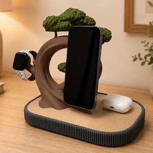 May include: A multi-device charging station featuring a brown tree-shaped stand with green foliage. The base has a tan, textured surface with circular patterns and a dark grey ridged edge. It holds a black smartphone, a smartwatch, and white earbuds.