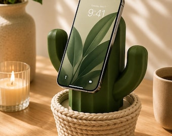 May include: A dark green cactus-shaped smartphone stand featuring a base wrapped in thick, cream-coloured rope. The stand holds a smartphone with a screen displaying the time 9:41 and a date of Tuesday, May 7, against a green leaf wallpaper.
