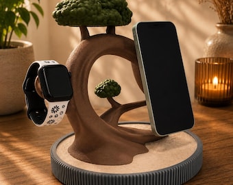 May include: A brown tree-shaped charging stand with green foliage, featuring a circular base with a textured edge. A black smartphone is attached to the right side, and a white smartwatch with a black floral pattern is attached to the left side.
