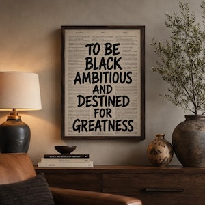 Peut inclure: Une œuvre d'art murale rectangulaire encadrée présentant un fond de page de dictionnaire vintage avec le texte noir en gras : TO BE BLACK AMBITIOUS AND DESTINED FOR GREATNESS. L'impression est insérée dans un cadre en bois brun foncé.