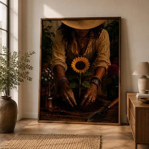 May include: A framed wall art print depicting a person wearing a straw hat and a tan shirt, planting a bright yellow sunflower in dark soil. The person wears multiple bracelets and rings on their hands, with a small metal trowel nearby.