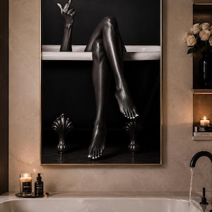 May include: A framed wall art print featuring a black and white photograph of a person with dark skin sitting in a white bathtub. The person has their legs crossed and is extending one arm upward with a finger raised. The bathtub has dark feet.