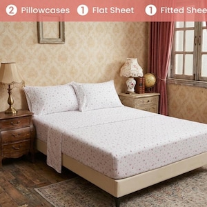Pode incluir: Um conjunto de lençóis composto por duas fronhas, um lençol plano e um lençol com elástico, todos decorados com um padrão floral de pequena escala em rosa e verde sobre fundo branco, exibido numa cama com duas almofadas e um colchão.