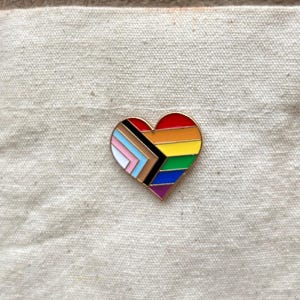 Peut inclure: Une broche en émail en forme de cœur arborant le motif du drapeau Progress Pride. Elle présente des bandes horizontales rouges, orange, jaunes, vertes, bleues et violettes, avec un chevron sur la gauche composé de blanc, rose, bleu clair, marron et noir.