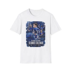 May include: White t-shirt featuring a graphic of a soccer player in a blue uniform. The graphic includes the text "60 GRAND, 60 GRAND SEAMUS COLEMAN" in white and blue. The shirt is a crew neck.